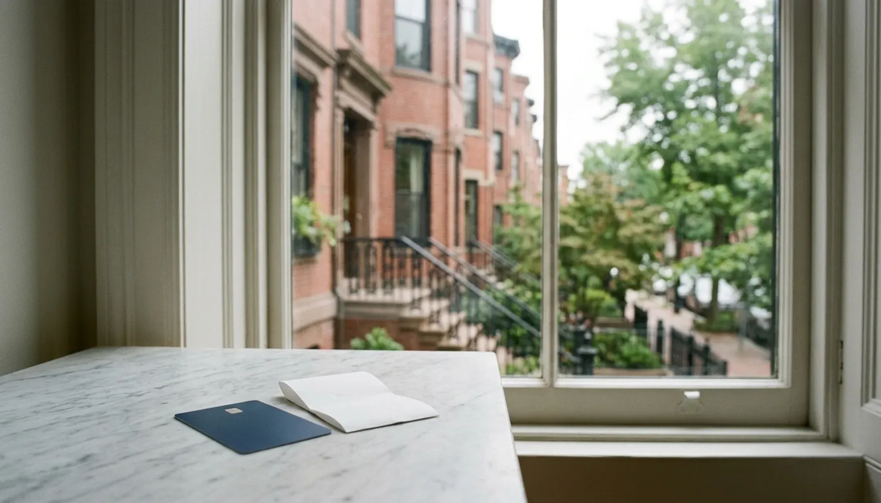 Debit card and folded receipt slip on marble by a window facing Boston brownstones, for property management in Boston MA fees