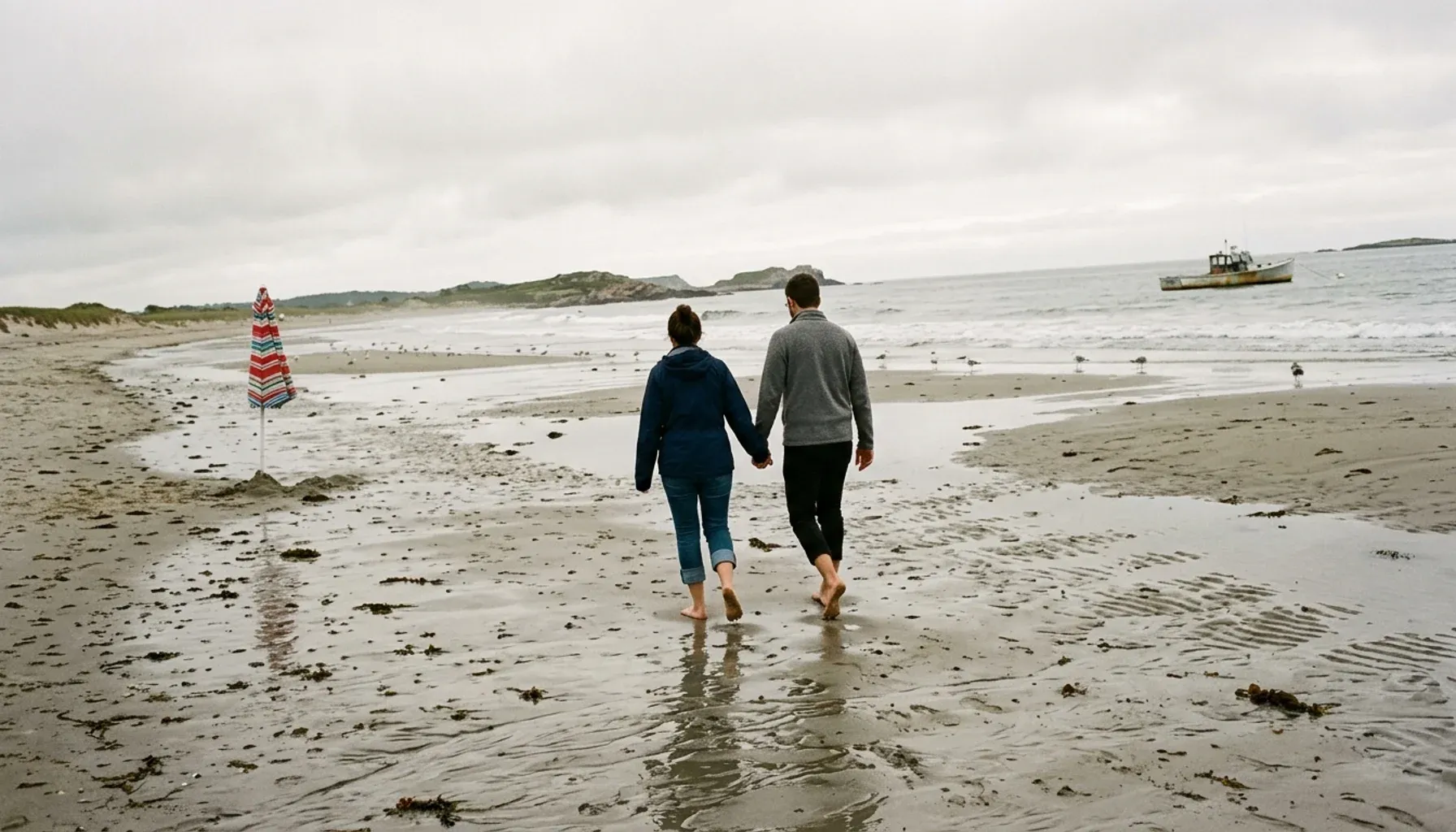 Two people walking along a sandy beach beneath an overcast sky
