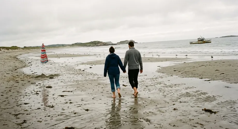 Two people walking along a sandy beach beneath an overcast sky