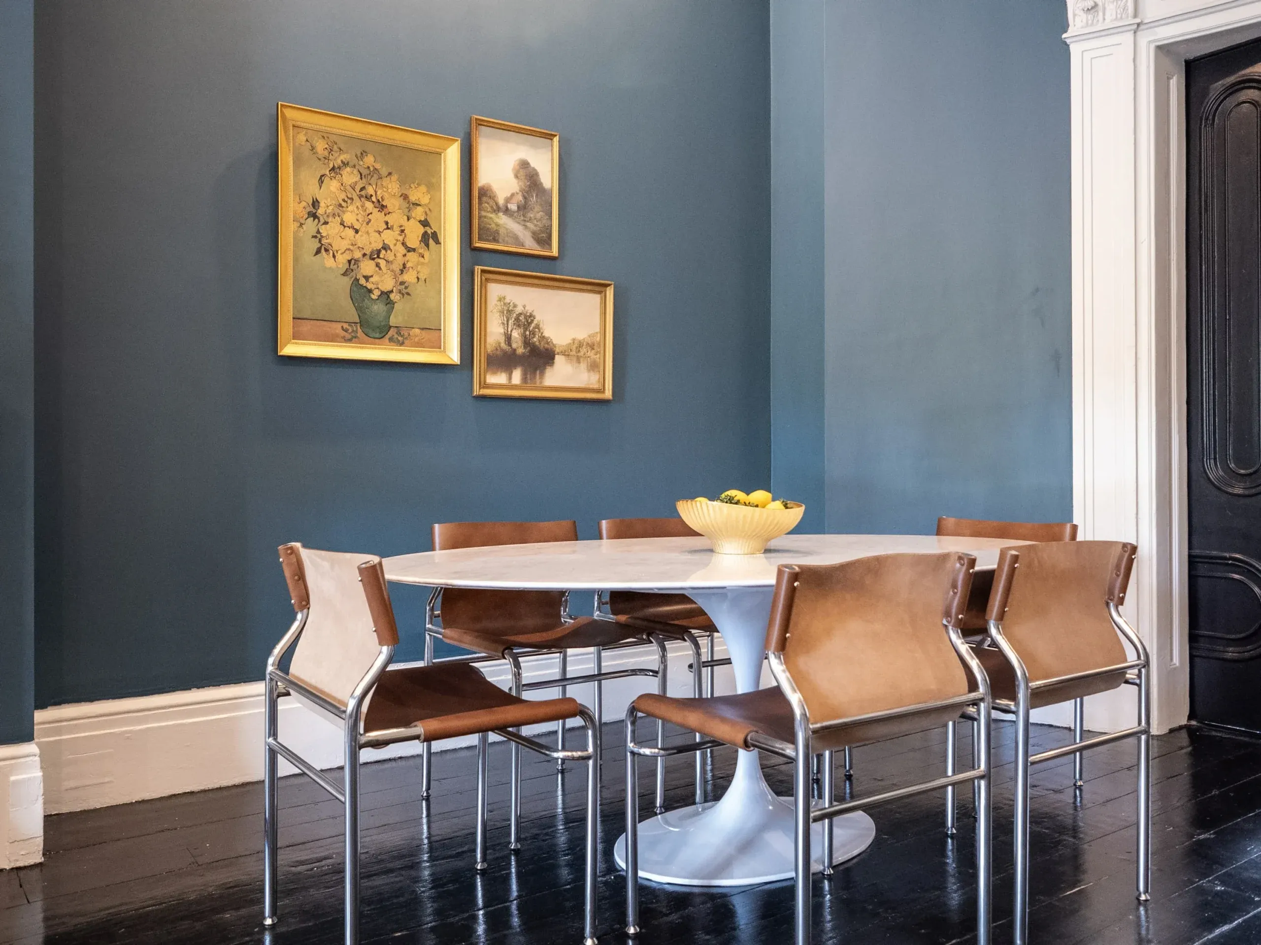 Dining table and tan chairs against a blue wall with framed artwork
