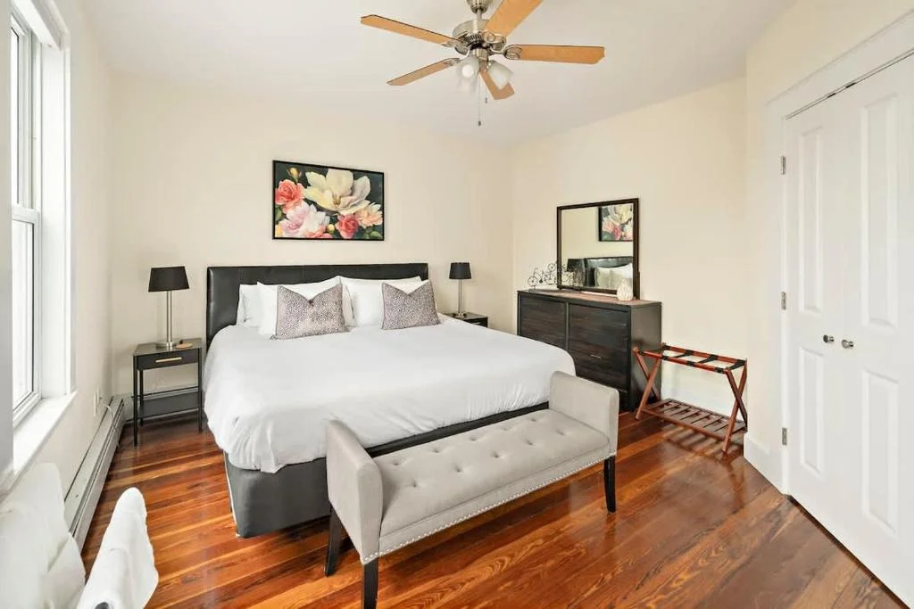 Bright bedroom for a romantic getaway in Cambridge: queen bed with black headboard, white linens, hardwood floors, and