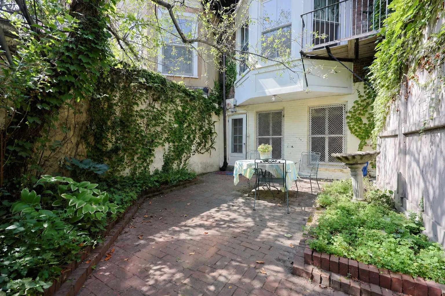 Private brick patio with ivy-covered walls and outdoor dining table, leading to a brownstone townhouse in a Boston, MA rental