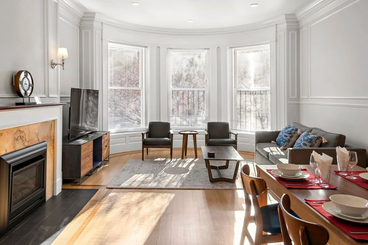 Open-concept living room with bay windows, hardwood floors, fireplace, and neutral furnishings in a Boston South End