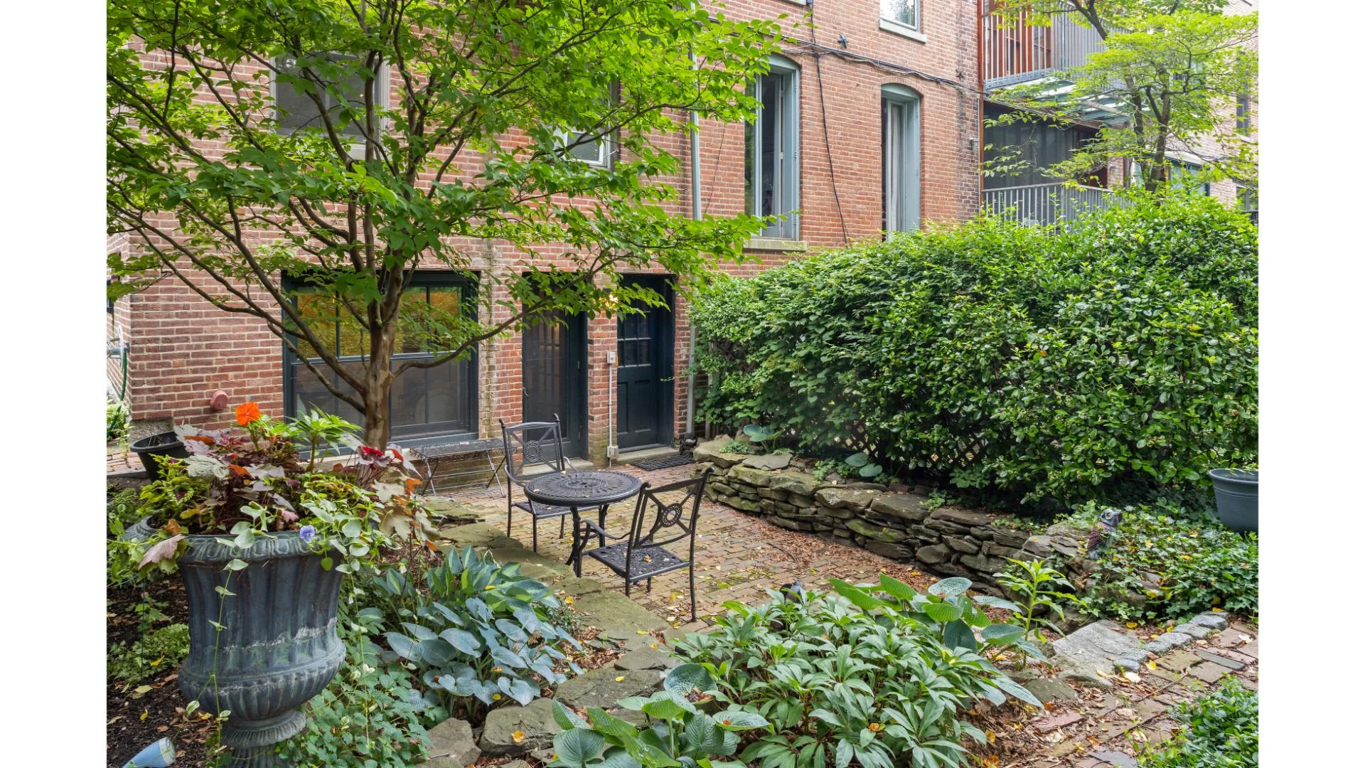Private patio with wrought iron seating, flowering planters, and ivy-covered brick walls in a Boston vacation rental, Enjoy