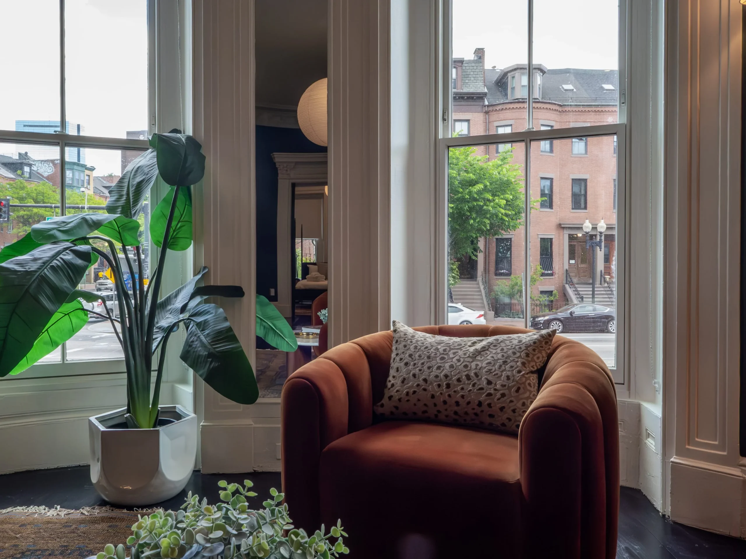 Modern penthouse living room with rust velvet chair overlooking Boston brownstone street architecture