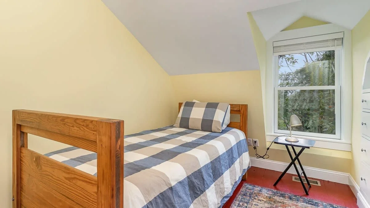 Bright bedroom with navy striped bedding, wooden single bed, skylights and yellow walls at a Gloucester, MA rental by South